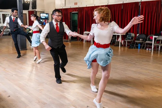 Two couples enjoying a swing dance at Midtown Stomp, with a smiling couple in a red tie and light blue skirt in front.