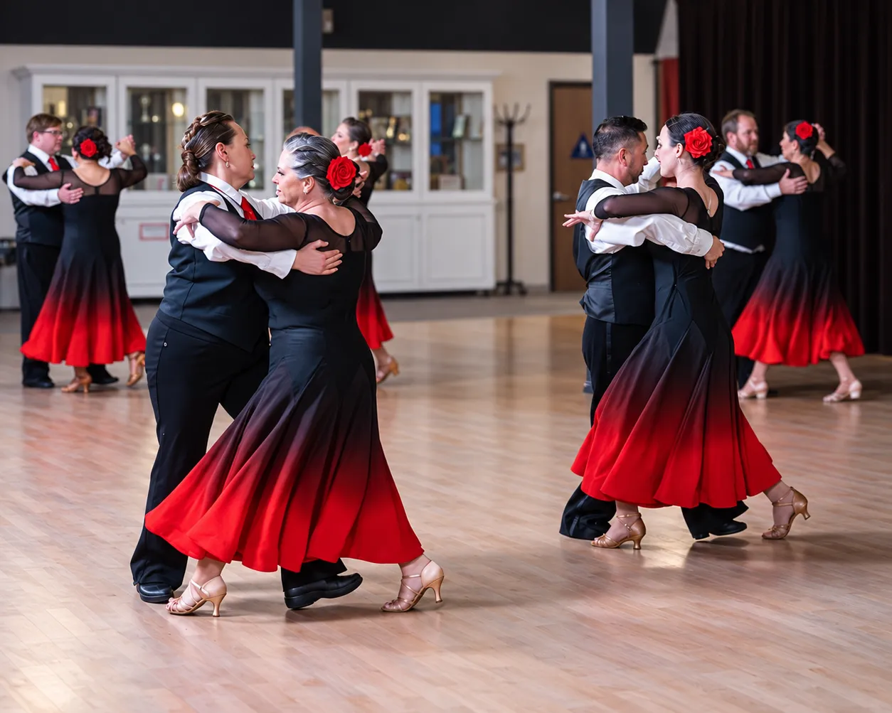 Couples in black and red gowns dancing on the Spotlight Ballroom floor