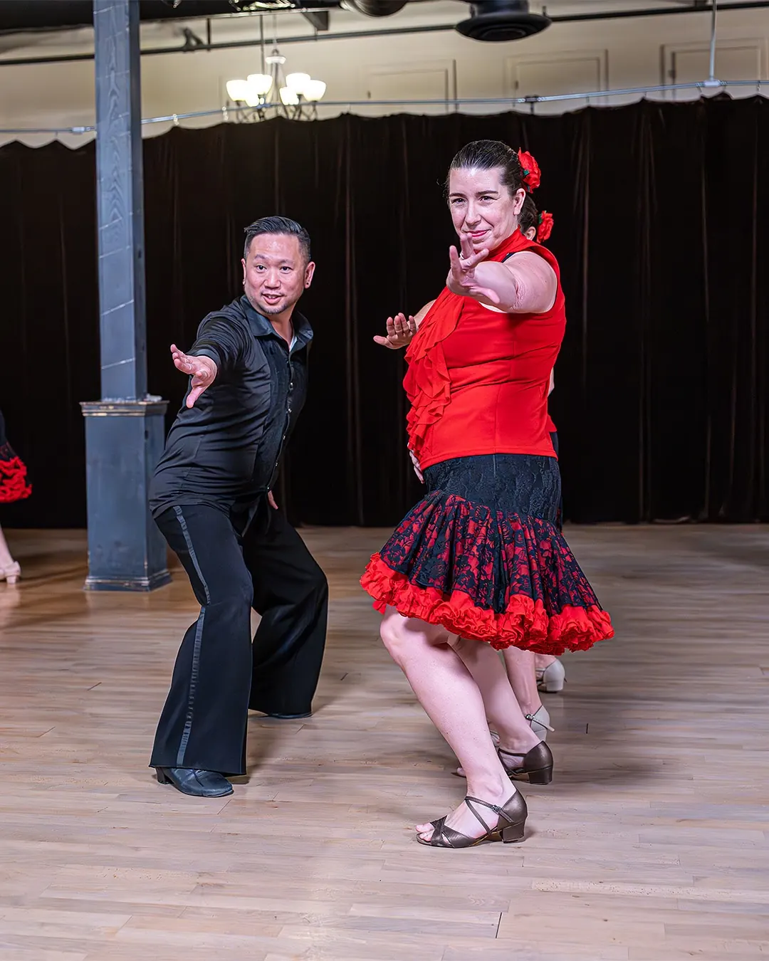 A Latin couple strikes a dramatic pose, her in a red top and ruffled skirt.