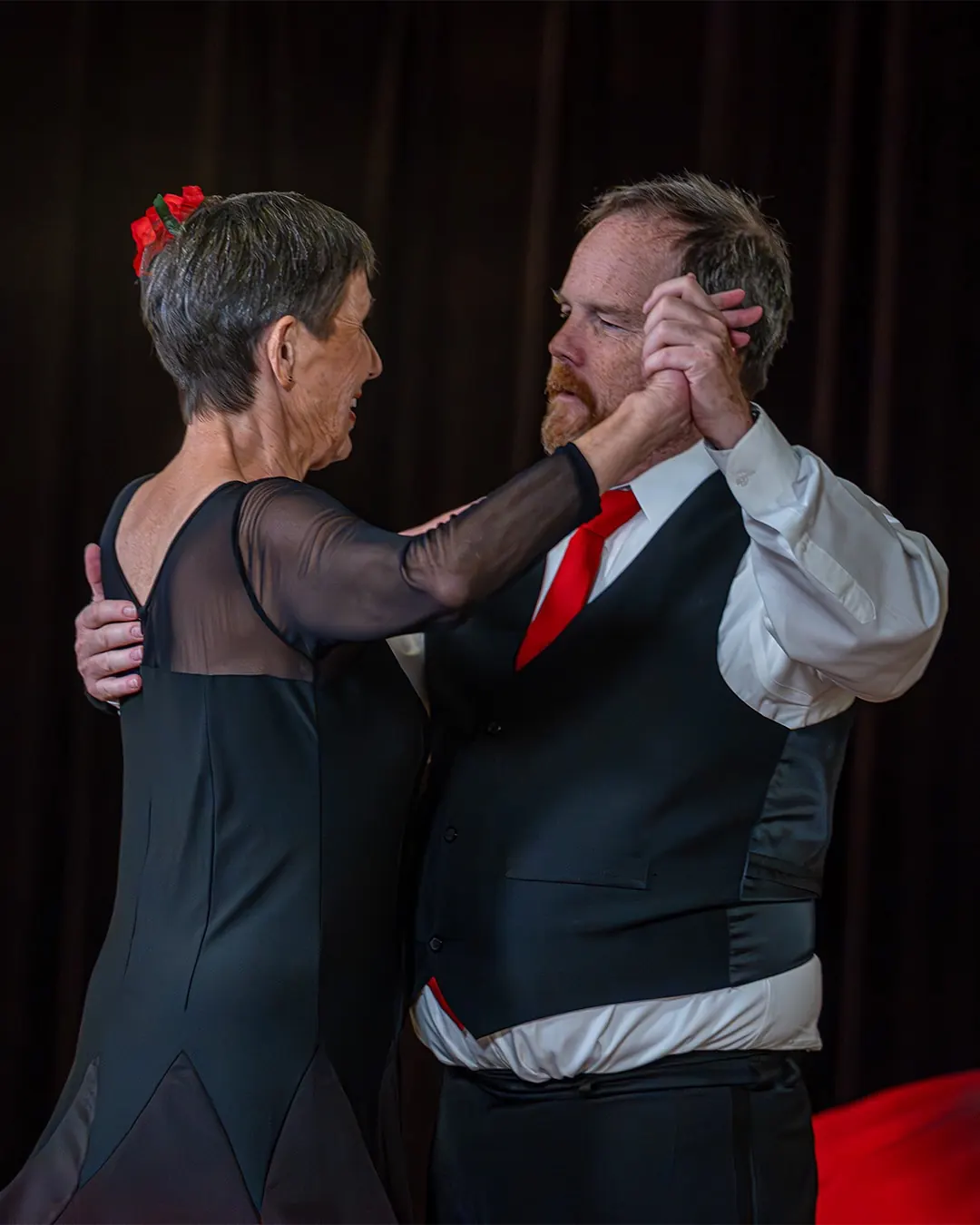 An older couple dances in a close ballroom hold, smiling.