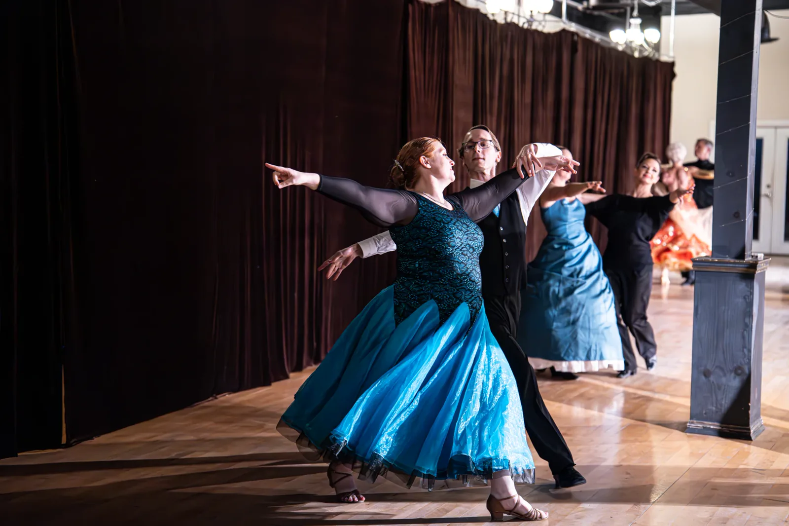 Couple in a smooth ballroom hold at Spotlight Ballroom, the woman in a turquoise gown with arms extended.