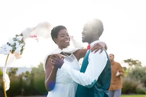 Smiling newlyweds embrace and sway together outdoors at sunset