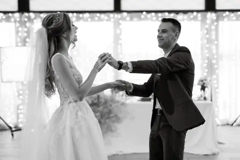 Black and white photo of a bride and groom holding hands and laughing under string lights